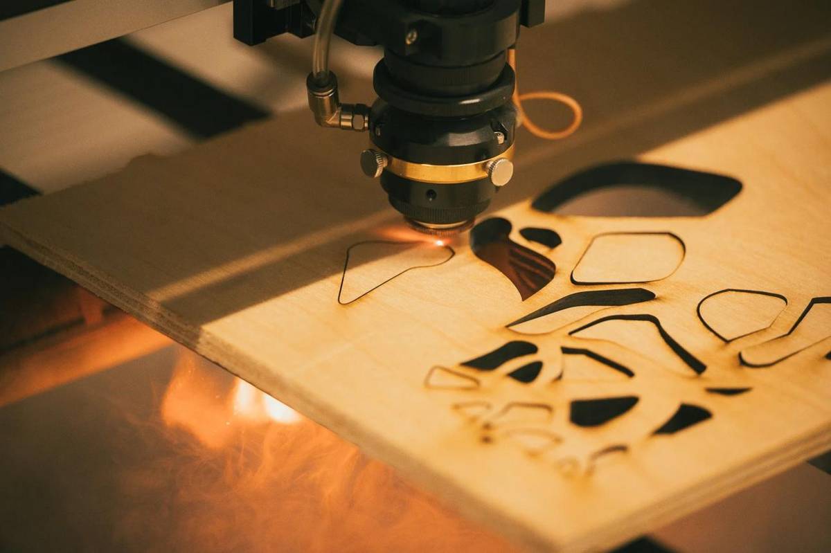 A laser head cutting shapes out of a sheet of birch plywood